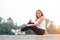 Portrait of beautiful young woman in white t-shirt and black trousers sitting in nature at sunset