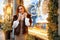 Portrait of a beautiful young woman who poses on the street near the elegantly decorated Christmas window, festive mood