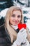 Portrait of a beautifull smiling woman in winter forest holding red Valentine`s heart in the hands.