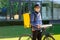 Portrait of bicycle courier with yellow bag and bike. Man in helmet and glasses holding pizza box