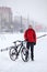 Portrait of bicyclist man standing with his bike on snowy path lane, winter bicycling in city during snowfall