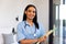 Portrait of biracial happy female physiotherapist with report and stethoscope standing at home