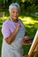 Portrait of biracial senior woman with short hair wearing apron holding brush and palette in yard