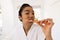 Portrait of biracial woman in bathrobe brushing teeth in sunny bathroom