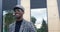 Portrait Black young man in fashionable outfit coat with animal print, turtleneck, cap and glasses, standing on city