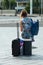 Portrait of blond girl with blue dress and phone waiting with suitcase in front of the train station