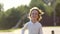 Portrait of blond little cute boy running in summer day and smiling. Child having fun outdoors outside park garden