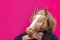 Portrait of blonde curly girl holding toy of horse`s head on bright pink background. Trend photo without face in minimal style