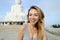 Portrait of blonde female person standing near white concrete statue of Buddha in Phuket.