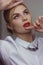 Portrait of a blonde girl with blonde hair in a white shirt in the studio room, with makeup and hairstyle, red lips and manicure,