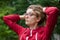 Portrait of blonde girl with hipster eyeglasses in dark red jacket making ponytail outdoors in the urban park