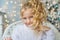 Portrait of blonde pretty little girl in white sweater on a chair in Christmas