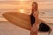 Portrait of blonde surfer woman on beach at warm sunset or sunrise. Surf girl with surfboard
