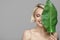 Portrait of blonde woman and green leaf. Organic cosmetics concept.