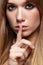 Portrait of blonde young woman with finger on lips. Female with