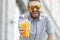 Portrait of a blurred stylish young hipster male with beard and mustache holding fresh orange juice in his hands