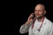 Portrait of a bold doctor with red stethoscope on dark background. Man talking on the smart phone, looking away from camera, smile