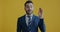Portrait of bored and annoyed businessman saying bla bla bla and making blabbing hand gesture on yellow background