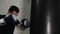 Portrait boxer man training blows on punching bag on white bricks wall background. Male fighter training on combat bag