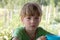 Portrait of boy with blue cup in hand sitting at table outside on garden background. Ecotourism, vacation in country, village.