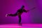 Portrait of boy, child, hockey player training, practising isolated over purple background in neon light. In action