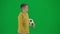 Portrait of boy on chroma key green screen. Schoolboy in casual walking holding football ball and looking around