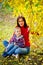 Portrait of a boy and mother in a red sweater sitting on the ground in an autumn Park near a yellow branch of a lime tree