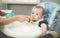 Portrait of boy sitting in highchair at kitchen and eating from