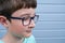 A portrait of a boy wearing glasses against grey blue plank painted wall with copy space, myopia, astigmatism and ophthalmologic