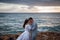 Portrait of a bride and groom on a background of sea, rocks and evening sky. The newlyweds are hugging. Wedding in