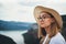 Portrait of brooding young girl with blonde hair in straw summer hat and hipster glasses on backdrop river natura mountain land