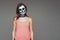 Portrait of brown-haired woman with terrifying halloween skeleton makeup in pink football and a tattoo on his arm over gray backgr