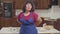 Portrait of brunette Caucasian mature woman putting on blue apron at the modern kitchen. Happy senior retiree preparing