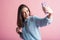 Portrait of a brunette girl on a pink background who takes a selfie on a smartphone.