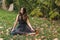 Portrait of a brunette Latina teen girl sitting with closed eyes on dry maple leaves in a park