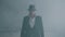 Portrait brutal gangster in fedora hat and classical suit walk from smoke. Slow motion. Abandoned dilapidated building