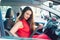 Portrait of business lady, caucasian young woman driver in red summer suit fastening car seat belt while sitting behind the wheel