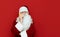 Portrait of a business Santa Claus talking on the phone and looking seriously at the camera on a red background. Serious Santa
