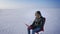 Portrait of businessman in warm coat and hood sitting in snow desert with laptop and stretching himself cheerfully.