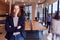 Portrait Of Businesswoman Standing In Busy Modern Open Plan Office  With Colleagues In Background