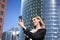 Portrait of businesswoman wave her hand at mobile phone camera, waves hand during video chat, stands in suit in city