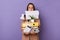 Portrait of busy funny woman with papers in mouth wearing beige jacket holding lot of documents folders isolated over purple