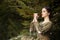 Portrait of Calm Caucasian Female in Old Medieval Green Dress Playing The Flute Against Firtrees Outdoors