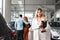 Portrait of a car sales manager woman. Auto dealership representative against the background of a couple who chooses a car