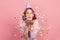 Portrait of carefree cheerful teenage girl in hoodie and party cone blowing heart shaped confetti, enjoying birthday or valentines