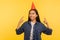Portrait of carefree excited girl in denim shirt pointing at funny party cone on head and smiling, celebrating success