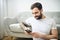 portrait of casual young man with beard and tattoo and white shirt sit on the sofa at home with cellphone