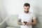 portrait of casual young man with beard and tattoo and white shirt sit on the sofa at home with cellphone