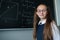 Portrait of a caucasian girl in glasses in the classroom. The schoolgirl answers at the blackboard.