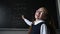 Portrait of a caucasian girl in glasses in the classroom. The schoolgirl writes the formula with chalk on the blackboard